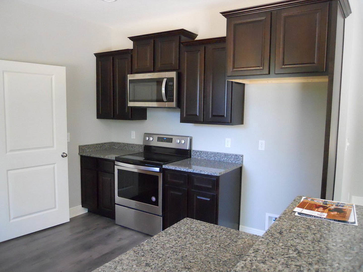 Kitchen with dark wood cabinets, granite countertops, stainless steel oven and stove, built-in microwave, white door, and modern appliances