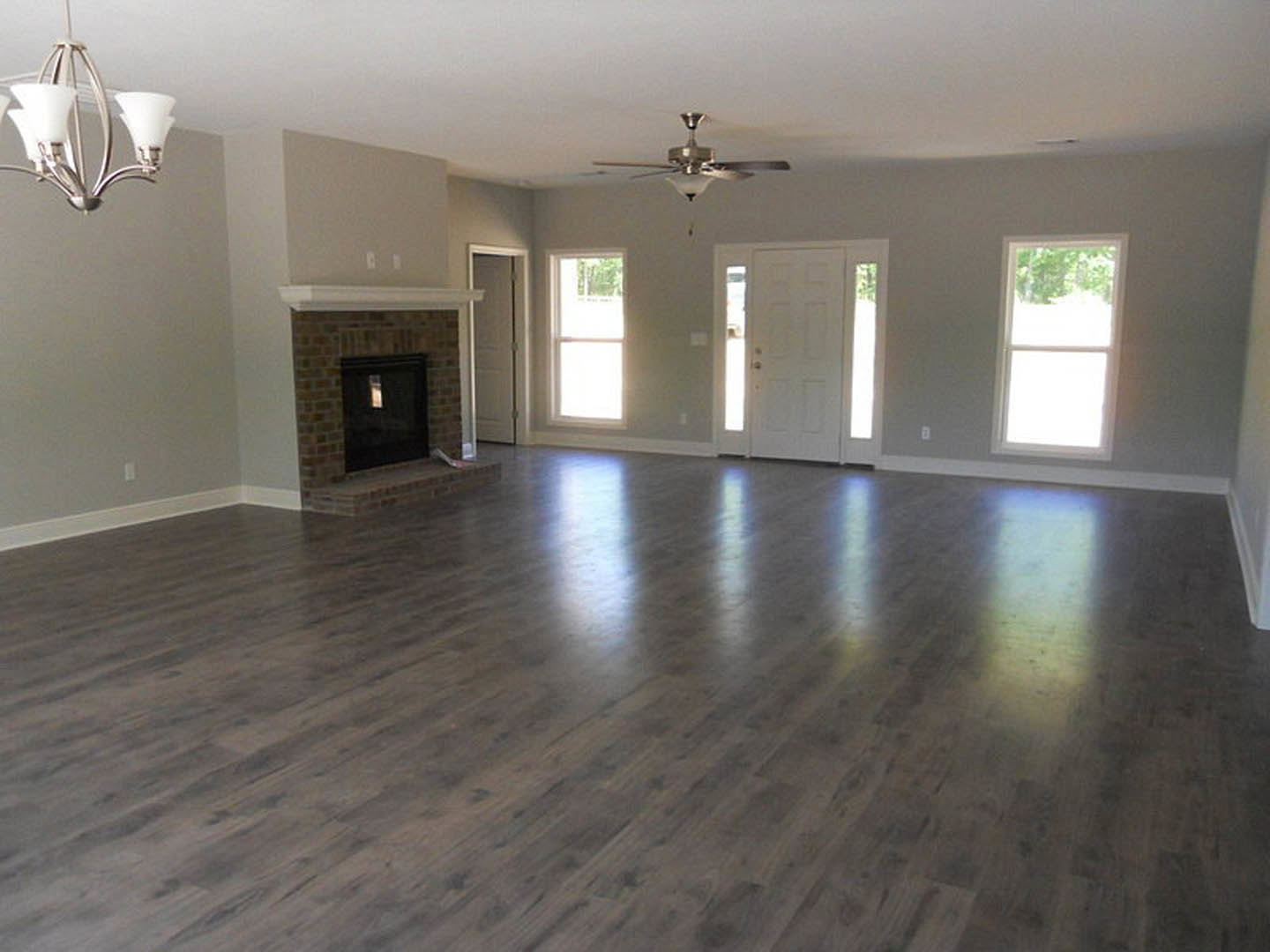Living room with hardwood floors, white-framed windows, stone fireplace, ceiling fan with light, and neutral walls