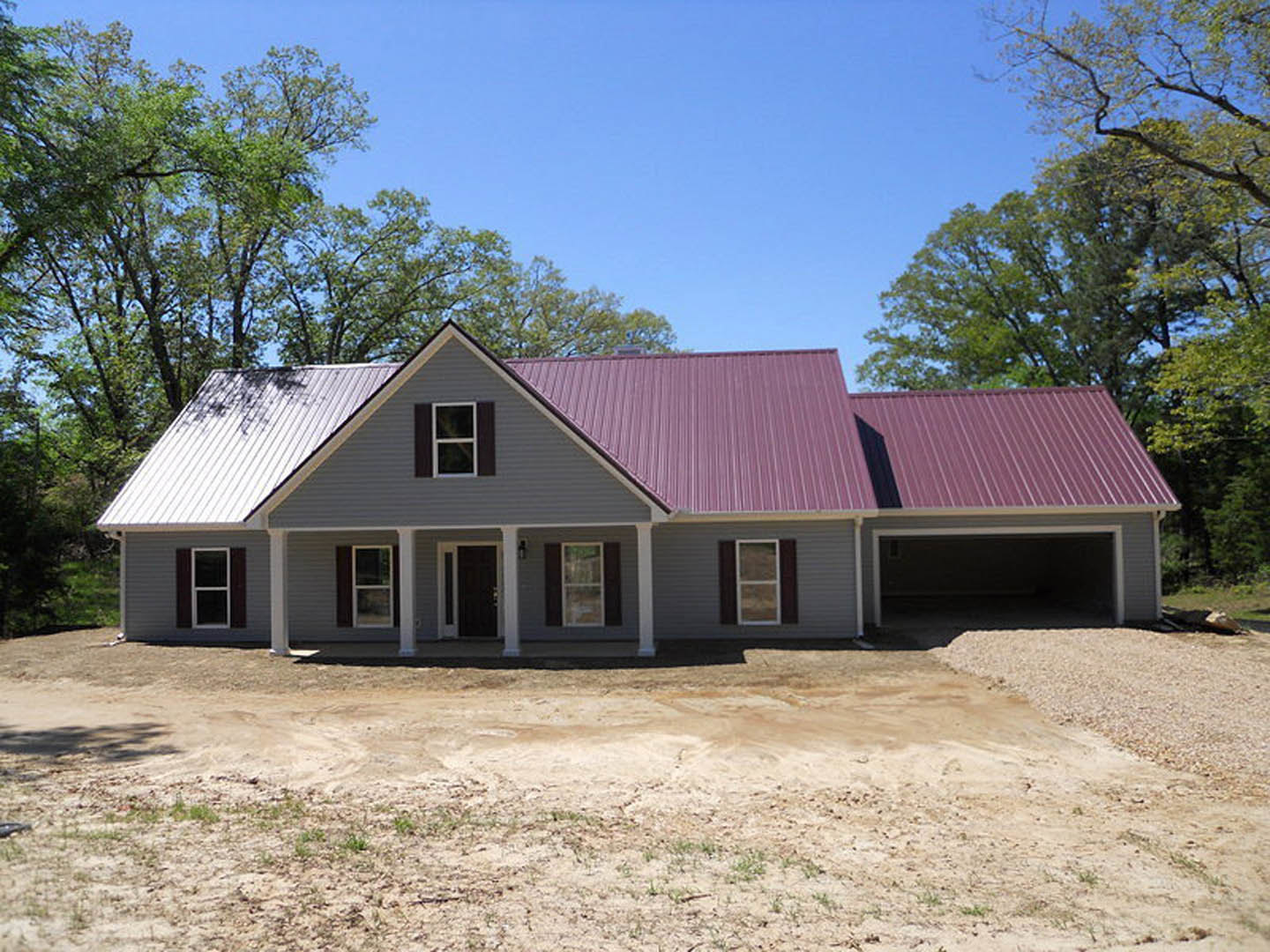 Two-story house with red gabled roof, white porch, and white-framed windows, surrounded by trees and blue sky