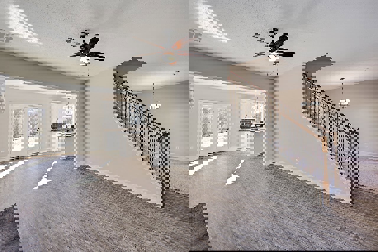 Open living area with wood flooring, white walls, ceiling fan with light, staircase featuring a chandelier, and double glass-paneled doors