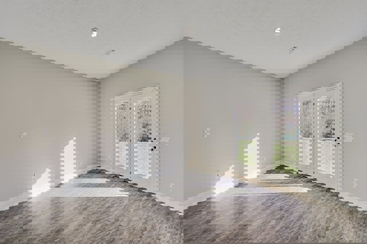 Wood floor with white stripes, double glass-paneled doors, white walls, ceiling light and fire alarm, window overlooking grassy field, interior molding details.