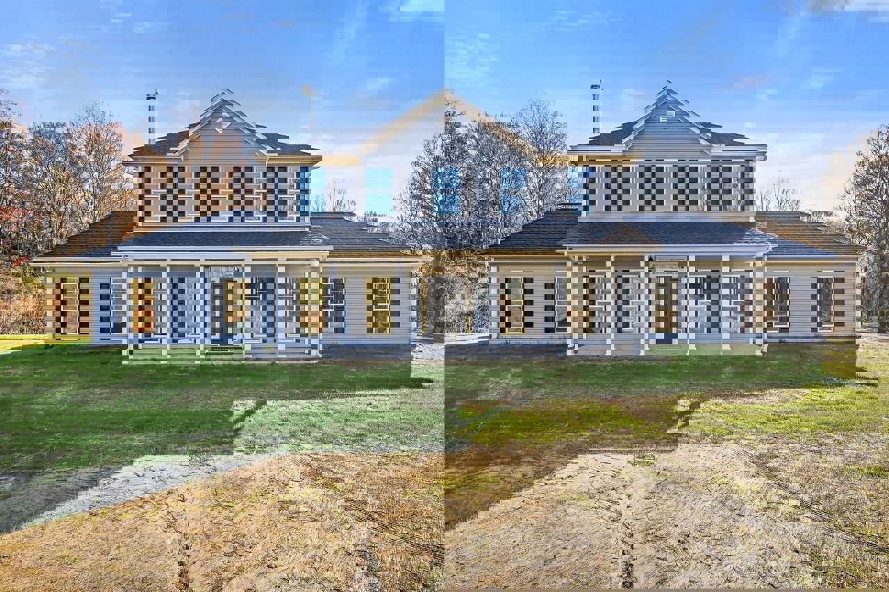 Spacious two-story home with grey roof, white columns, black front door with white trim, expansive windows, and manicured green lawn