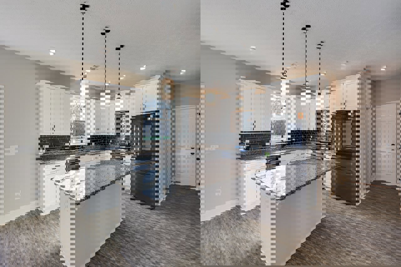 Modern kitchen featuring a black and white marble countertop, black refrigerator, white cabinetry with black knobs, window with hanging light fixture, and black support pole