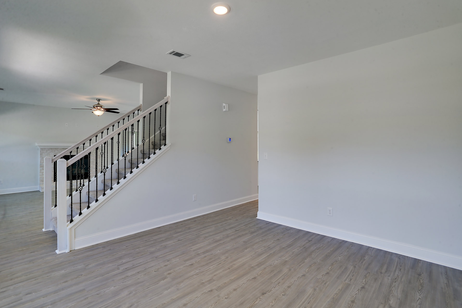 Open living area with wood flooring, white plaster walls, black metal staircase railing, and ceiling fan with light fixture