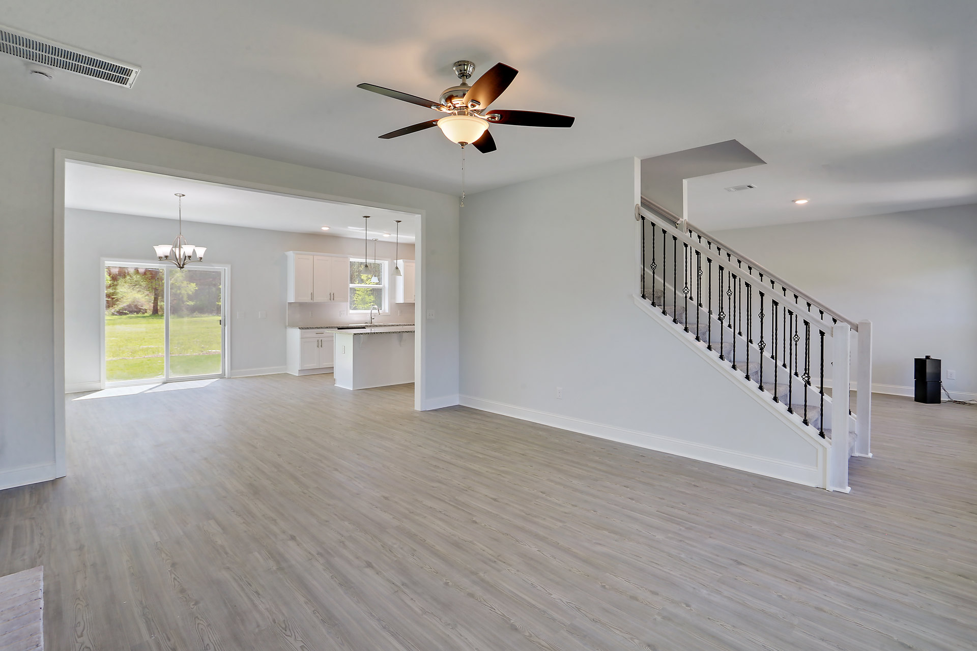 Open living area with wood flooring, white staircase featuring black railings, ceiling fan with integrated light fixture, neutral walls, and plaster ceiling.
