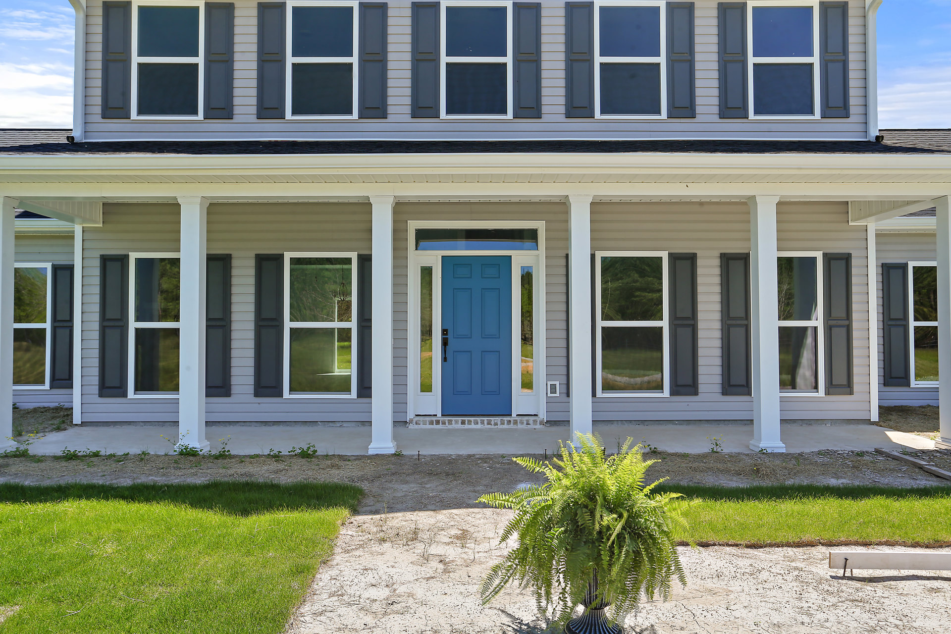 White house exterior with tall columns, blue front door with black handle and glass panels, white-framed windows, potted plant on porch, green lawn in foreground