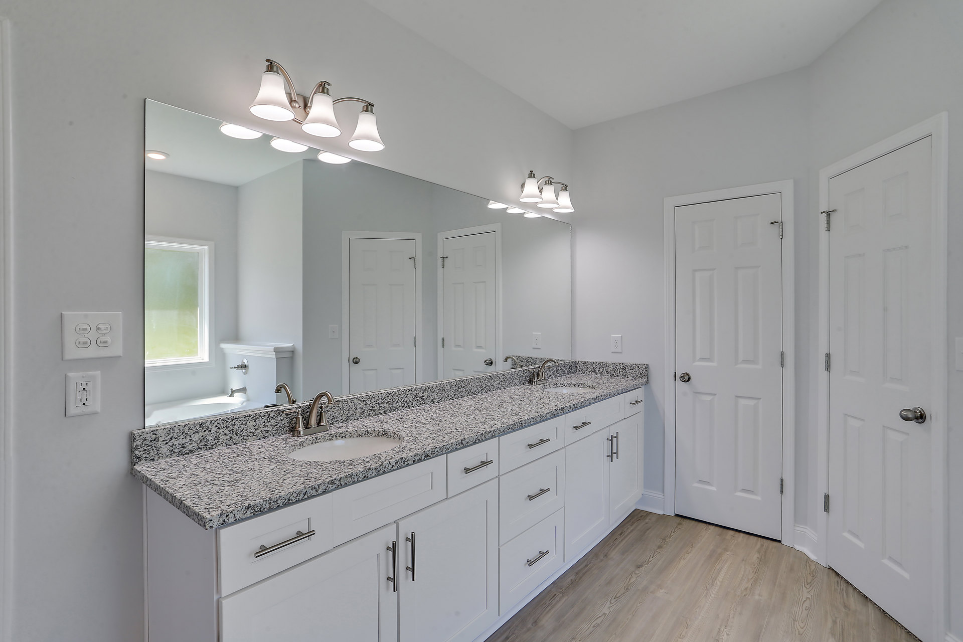 Bathroom with marble countertop, white cabinetry, undermount sink, silver faucet, white door with silver knob, wall outlet, and modern light fixture with white shade