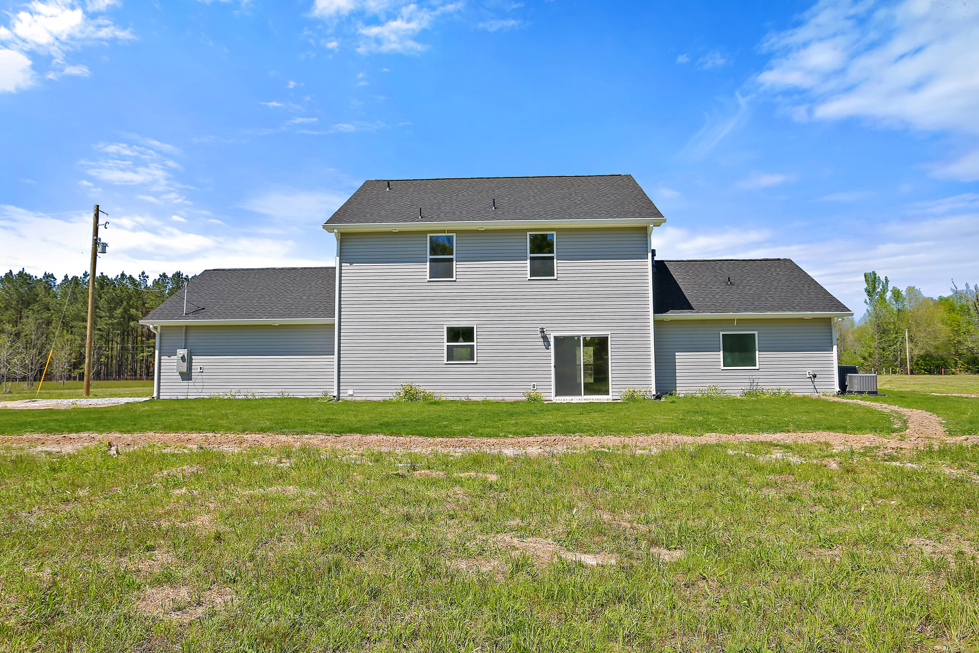 White farmhouse with gabled roof, large front windows, wooden door, and manicured green lawn bordered by trees under partly cloudy sky