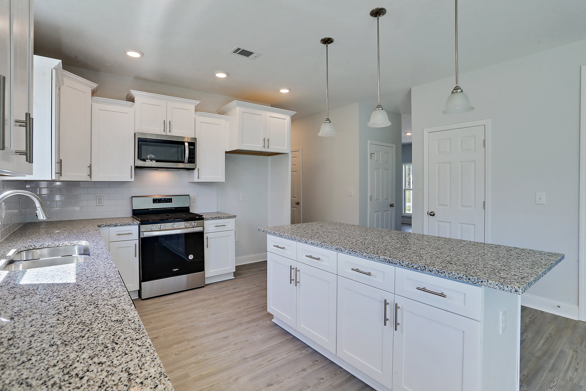 Granite countertops, white cabinets with silver handles, stainless steel stove with glass door, built-in microwave, metal fixtures, and undermount sink in a modern kitchen