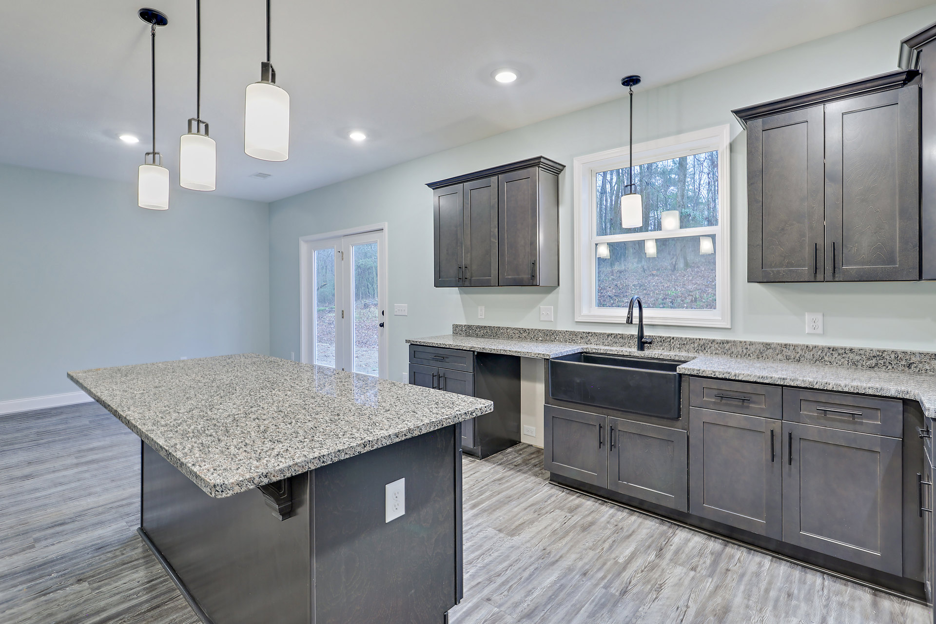 Granite countertops with undermount sink, white cabinetry, tile backsplash, stainless steel faucet, and modern light fixture in a custom kitchen