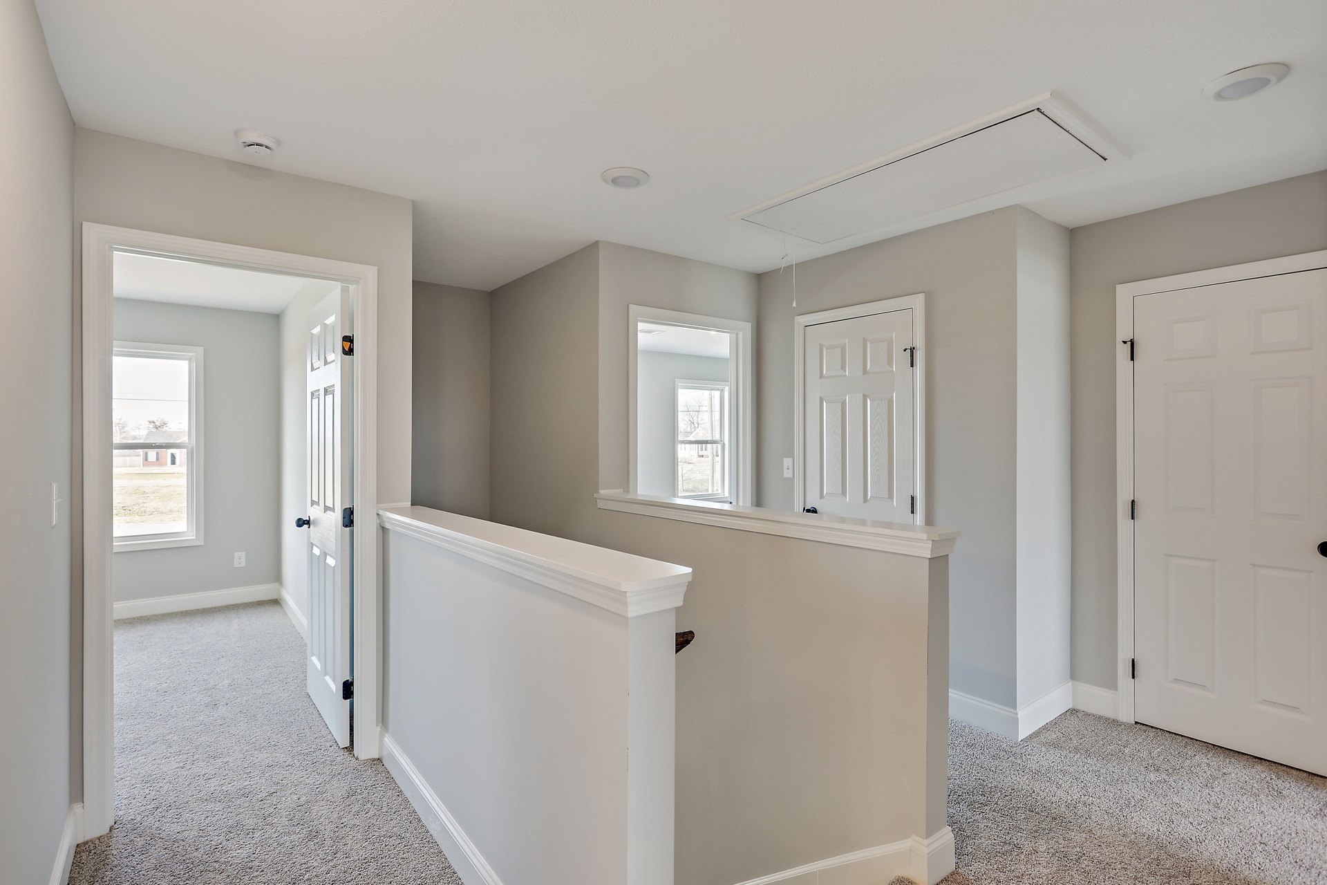 Hallway with white plaster walls, white door featuring black handle and cross design, white railing, tile flooring, ceiling, and window offering view of neighboring house and fence