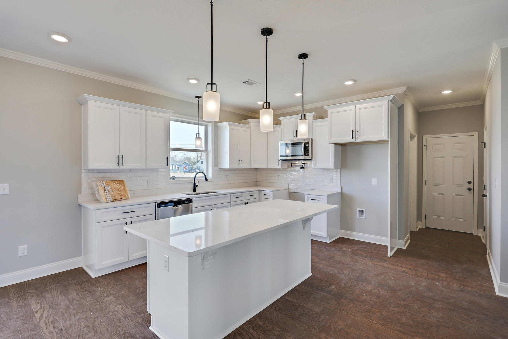 White kitchen with shaker cabinets, white island featuring a stainless steel dishwasher, black hardware on doors, wood cutting board wrapped in plastic, chrome faucet, and smooth