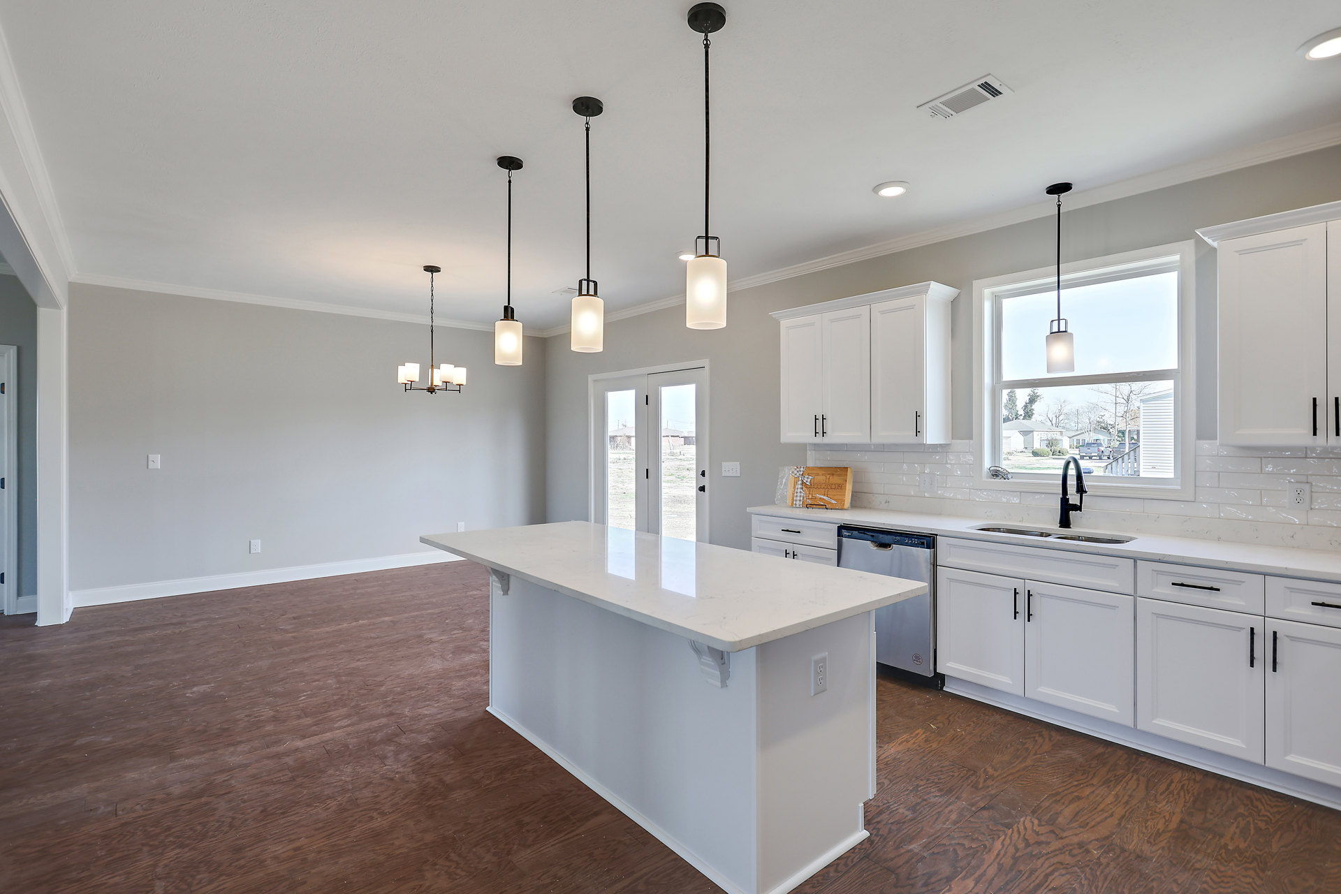 White kitchen island with waterfall countertop, wood plank flooring, white cabinetry, stainless steel sink, and recessed lighting.