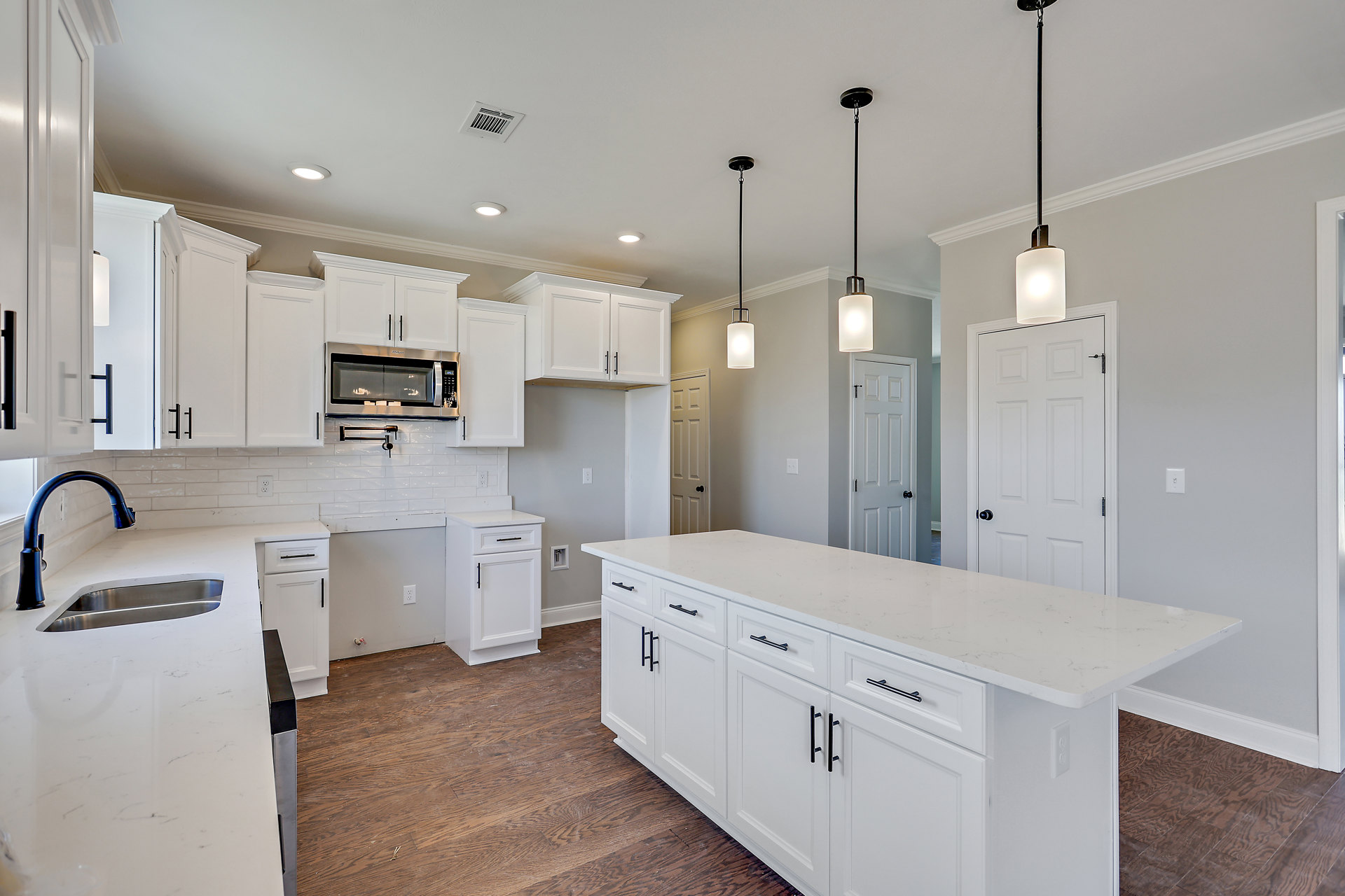 White kitchen with shaker cabinets, white quartz countertops, black hardware, built-in microwave, rectangular pendant light, tile backsplash, and stainless steel sink.