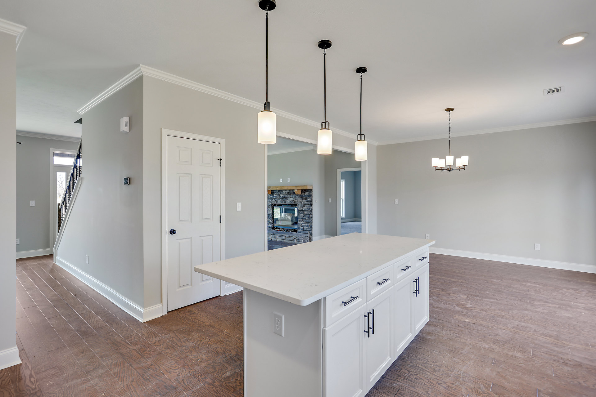 White kitchen island with black hardware, light wood flooring, white cabinetry, brick fireplace with inset box, recessed lighting, and plaster walls.