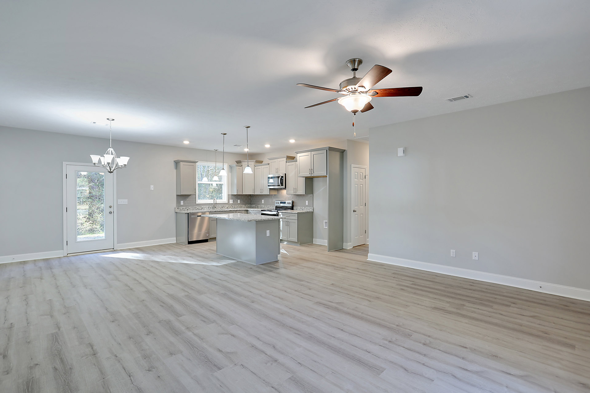 Open-concept kitchen and living room featuring a ceiling fan with light fixture, granite kitchen island, wood flooring, white walls, and a white door with window