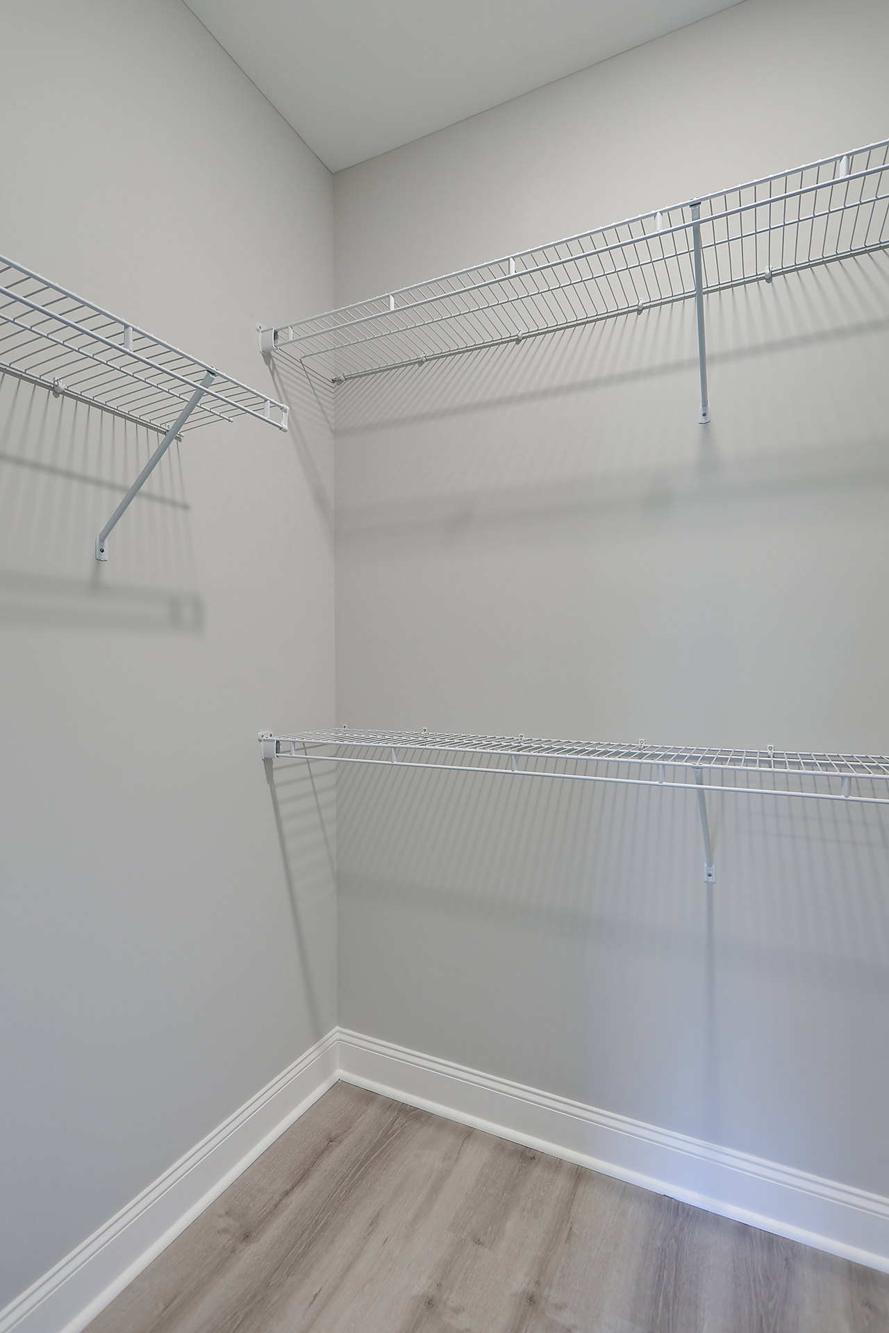 Built-in white wire shelving along plaster walls, brown wood flooring, and white baseboard trim in a small indoor room.