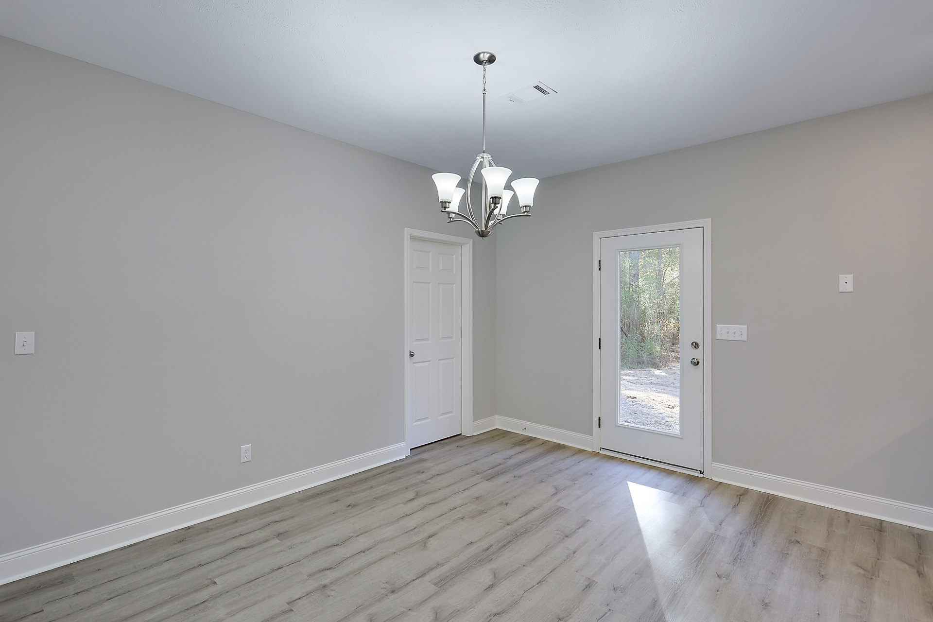 White-walled room with wood flooring, white door featuring a glass window and silver handle, ornate chandelier hanging from ceiling with decorative molding.