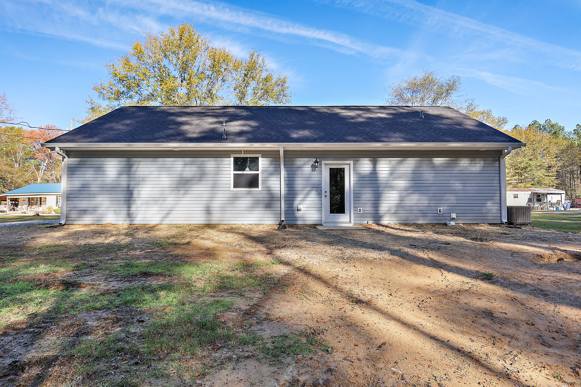 Two-story home with blue roof, white siding, glass-paneled front door, large window with cracked glass, grassy yard, mature trees in background