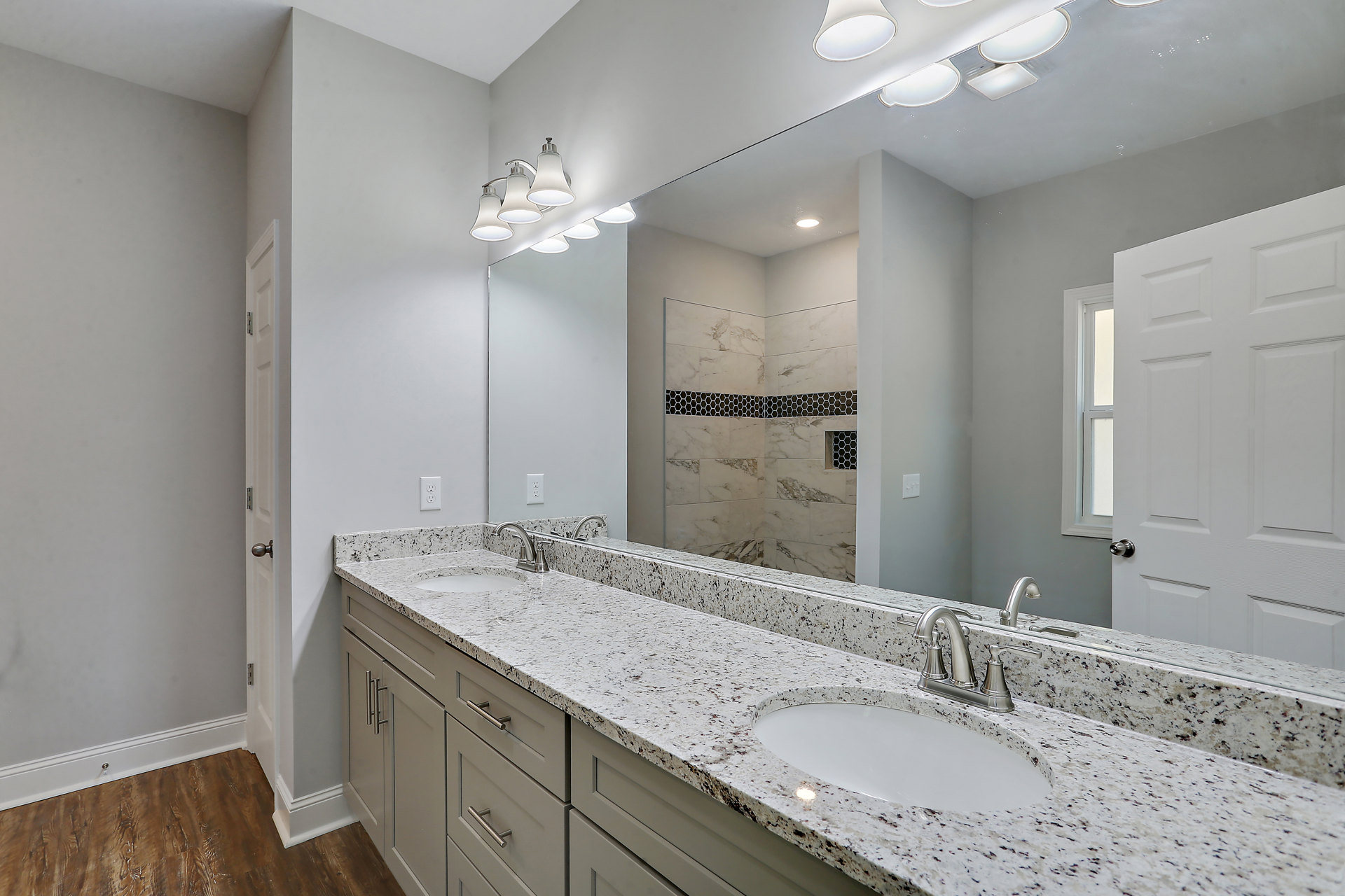 Bathroom with marble countertop, double white sinks, silver faucets, large wall mirror, white cabinetry, and tiled walls