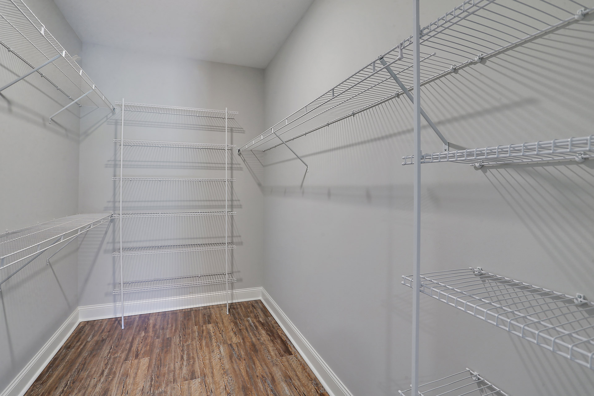 Wood floor with white trim, white wire shelves mounted on wall, plaster ceiling, and neutral painted walls in a closet or storage room.
