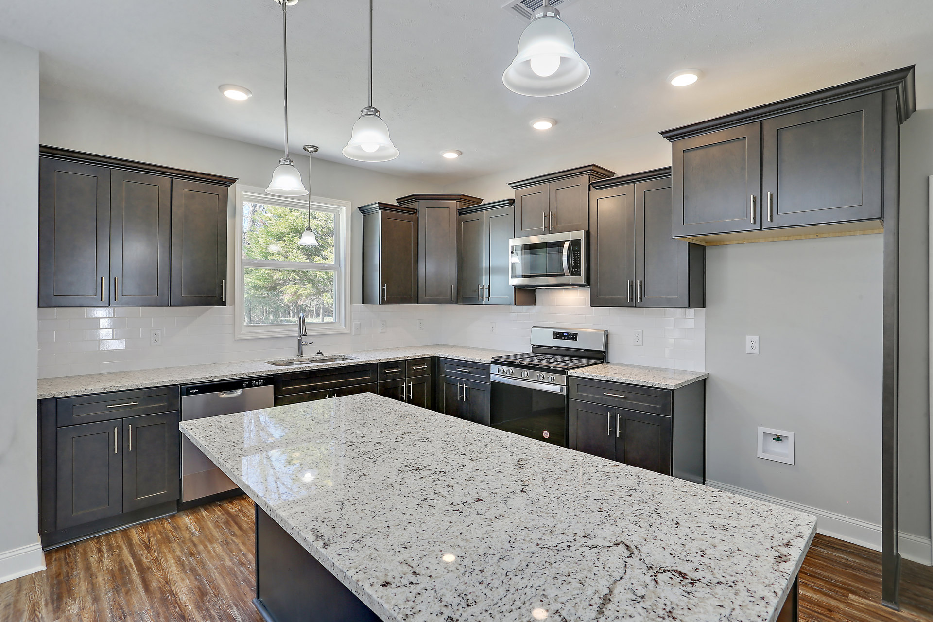 Granite countertops with black cabinetry, stainless steel microwave, white backsplash, ceiling light fixture, and undermount sink in a modern kitchen