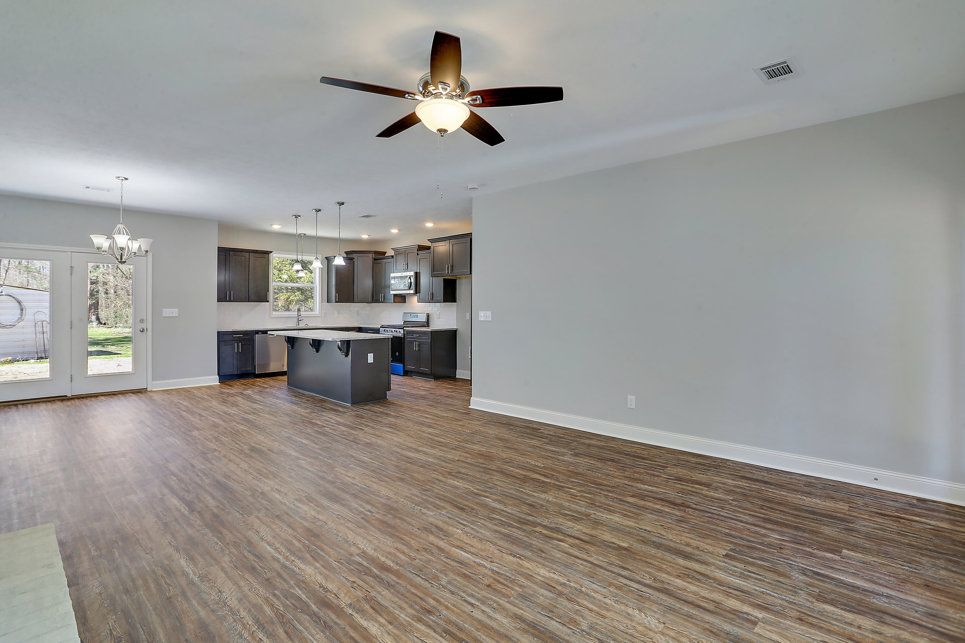 Open-concept kitchen and living room featuring a ceiling fan with light fixture, marble-topped kitchen island, wood flooring, and white walls