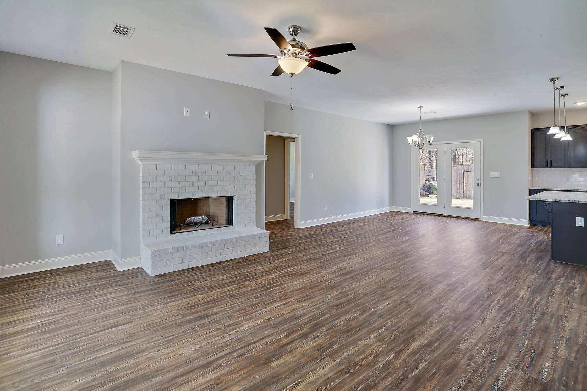 Living room with hardwood floors, white brick fireplace, ceiling fan with light fixture, mirrored door, and white decorative object inside fireplace