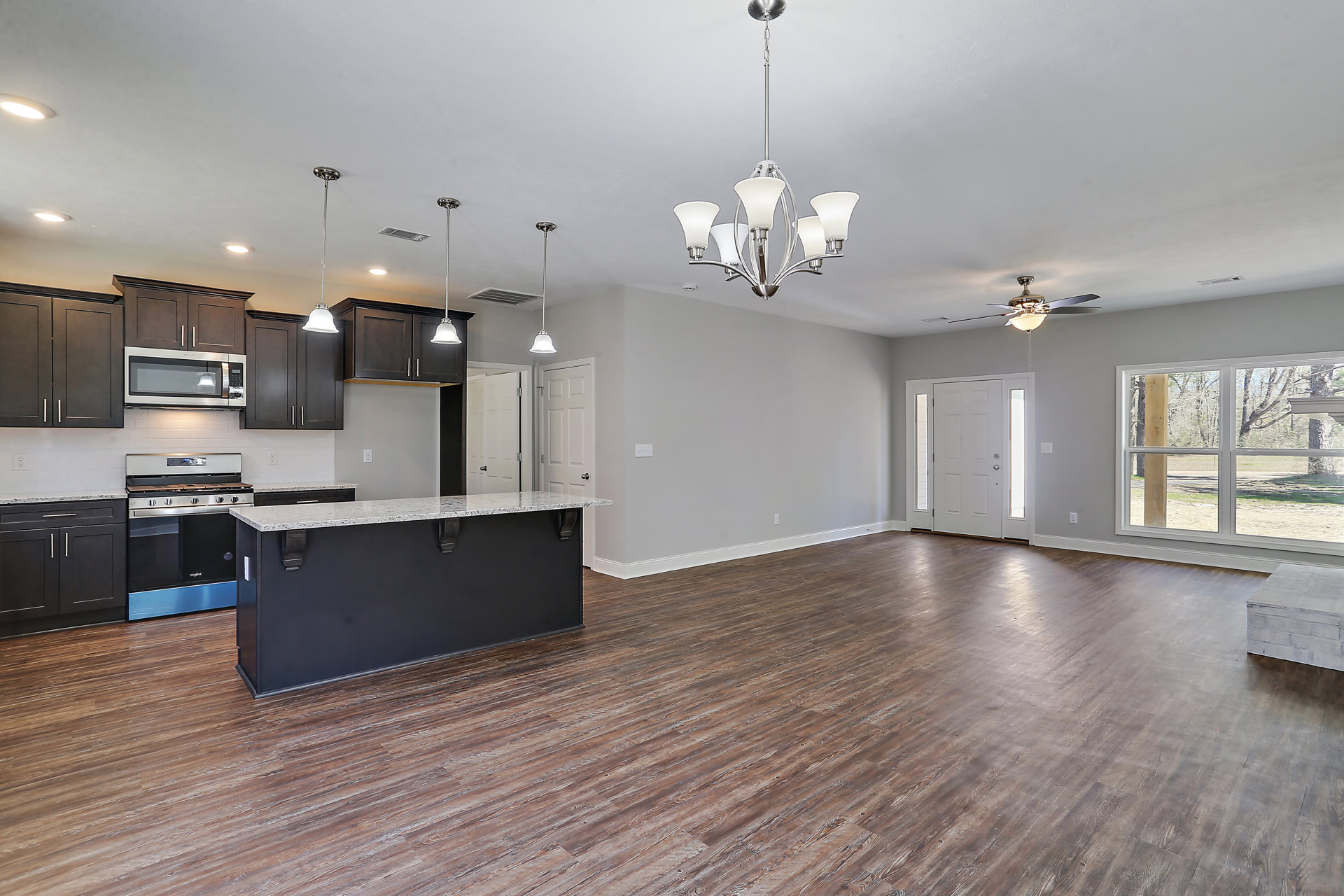 Open kitchen with white cabinetry, black backsplash, wood flooring, central island, pendant lighting, and modern appliances