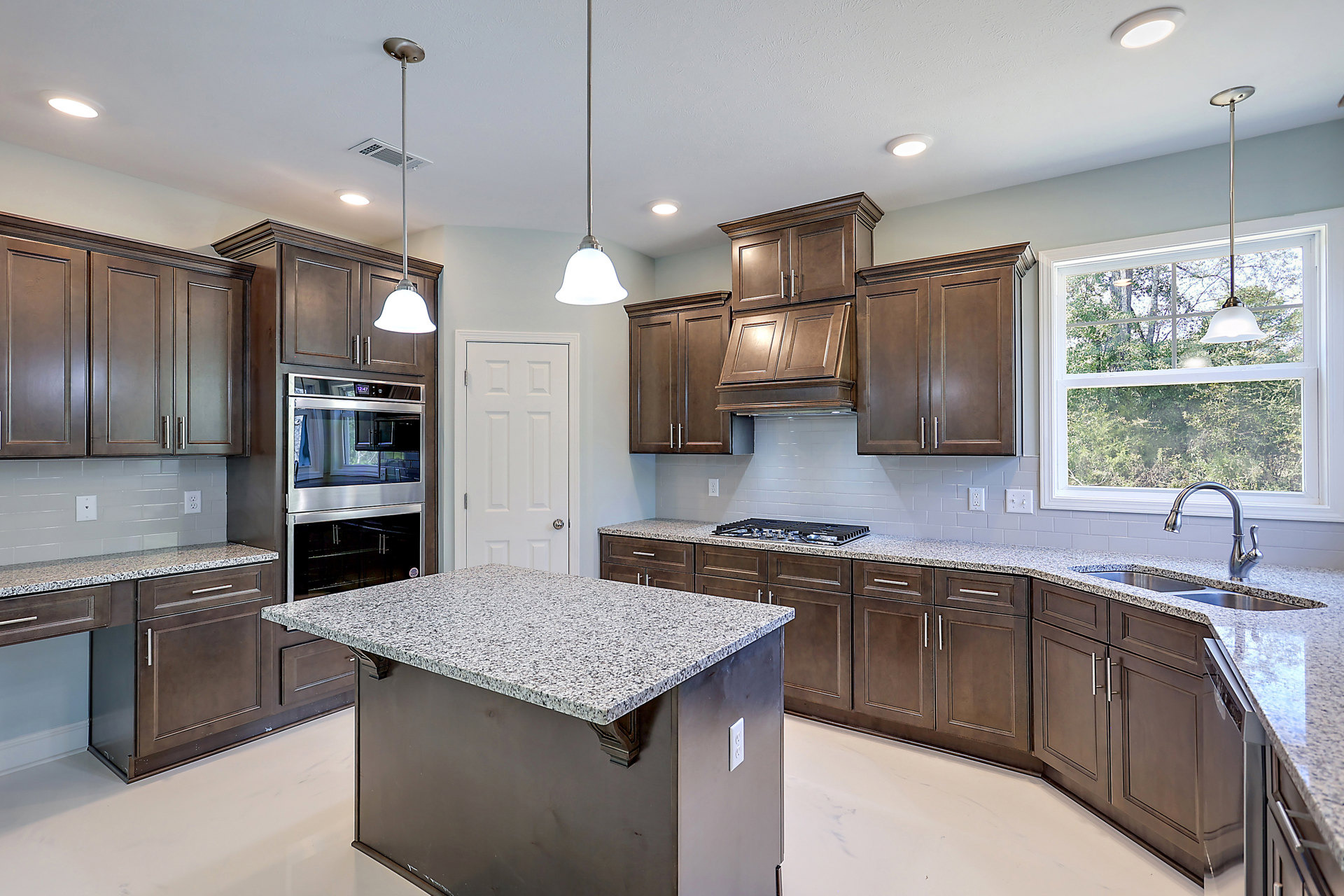 Spacious kitchen featuring a large white island countertop, stainless steel oven with glass doors, sleek cabinetry, ceiling vent, and modern fixtures.