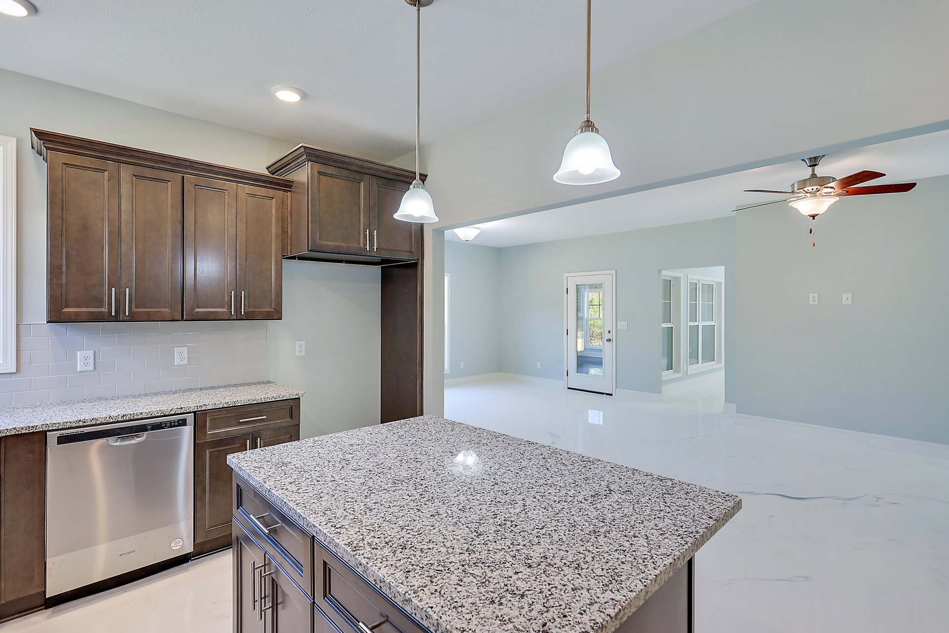 Marble island with speckled countertop, white cabinetry, stainless steel dishwasher, glass-paneled door, modern pendant light, and built-in sink in a contemporary kitchen.