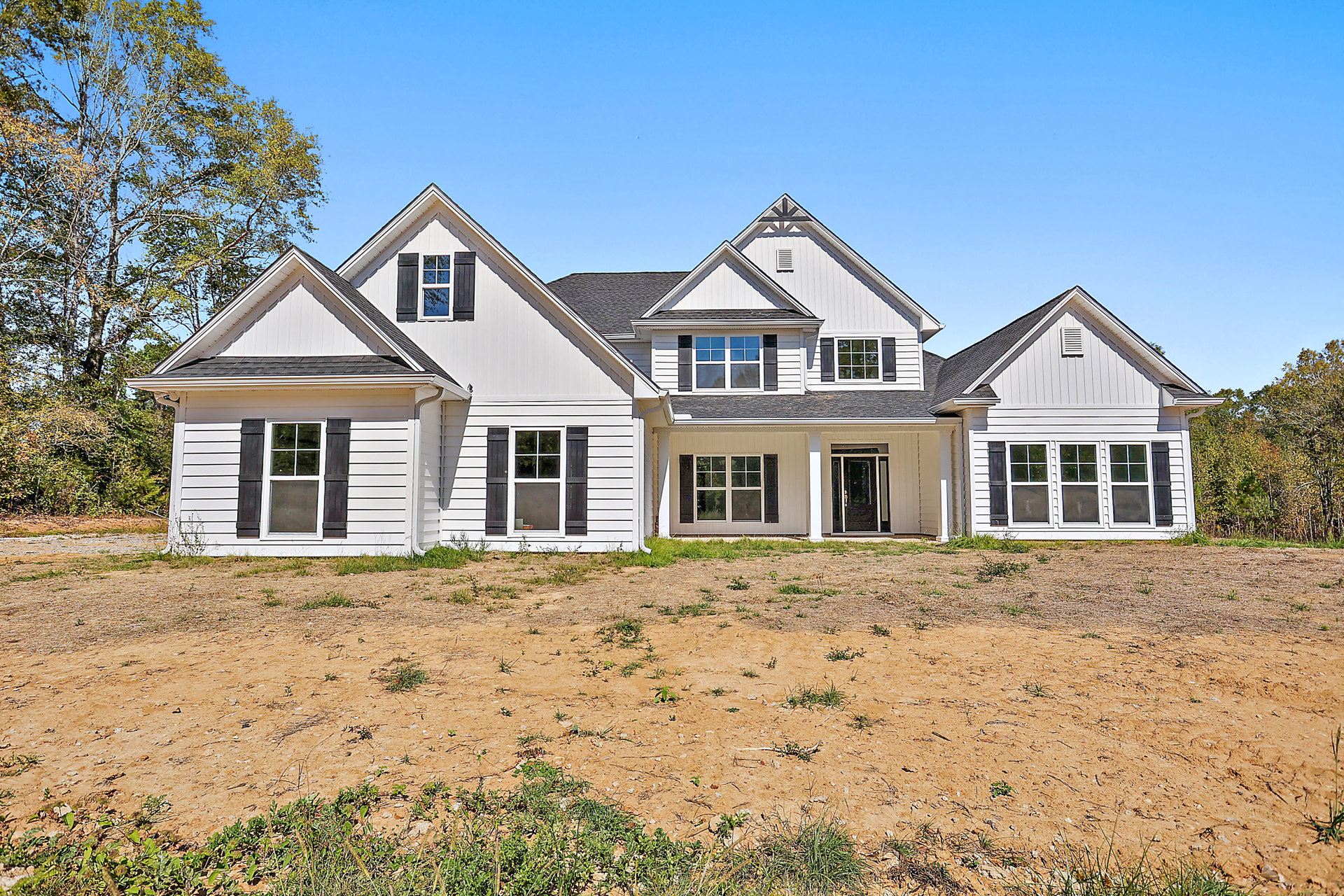 Two-story house with large gray roof, black front door with white trim, white-framed windows with black shutters, expansive grassy yard, dirt field, and Robert Frost Farm visible