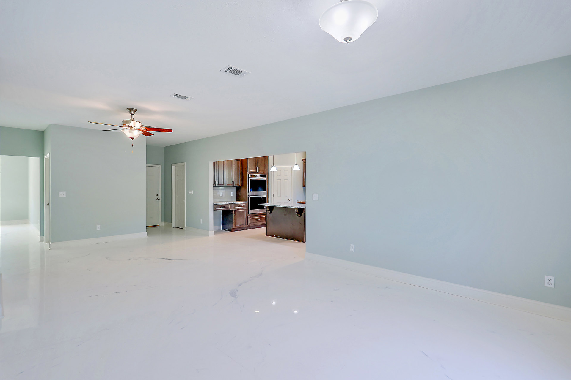 Open-concept kitchen with black marble countertops, stainless steel oven, white cabinetry, light-colored flooring, and ceiling fan with integrated light fixture