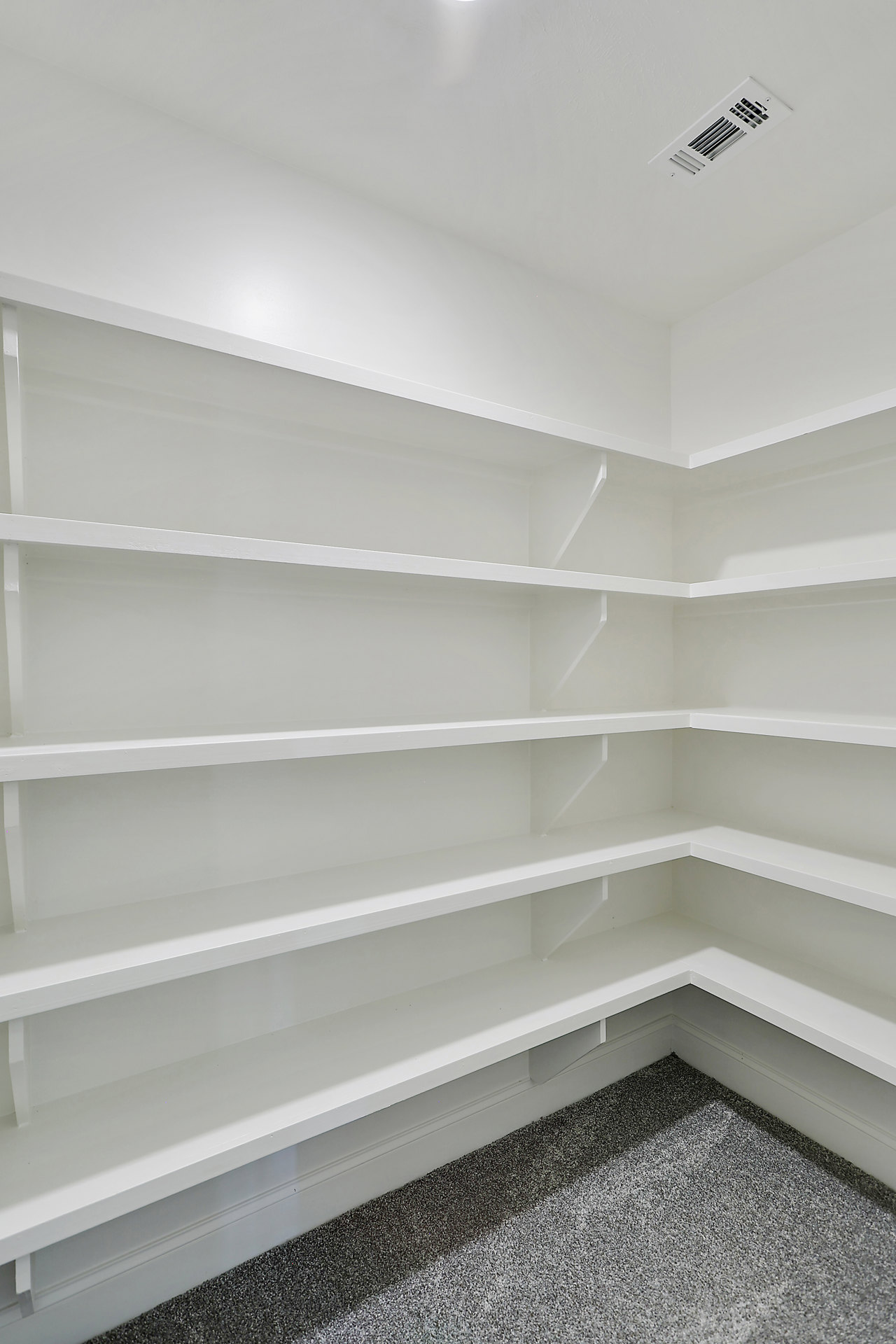 Built-in white shelves against a plaster wall, white ceiling with recessed vent and light fixture, carpeted floor in an empty room