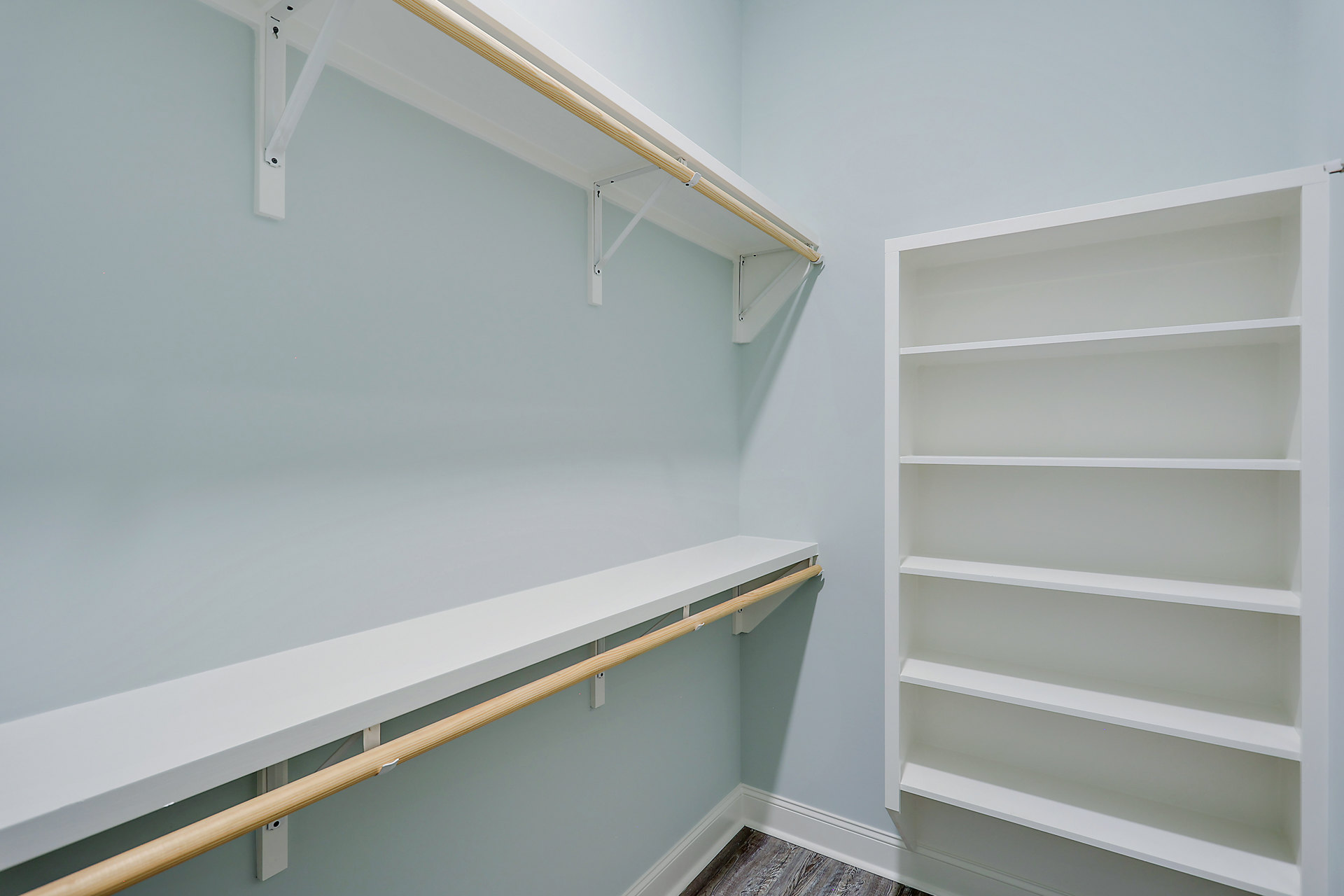 White built-in shelving unit with multiple open shelves and a wooden hanging bar against a plaster wall in a modern room.