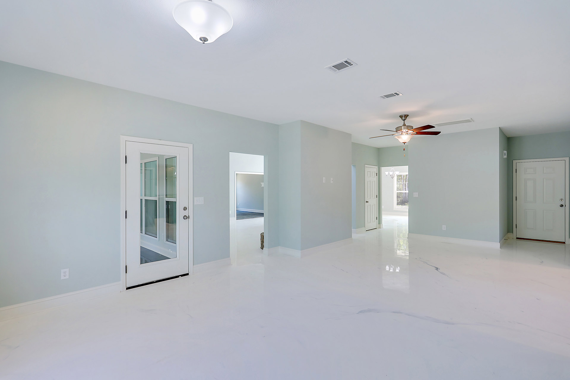 White walls and ceiling with a central ceiling fan and light fixture, white door featuring glass panels and a silver handle, ceiling vent visible near the fan, light-colored