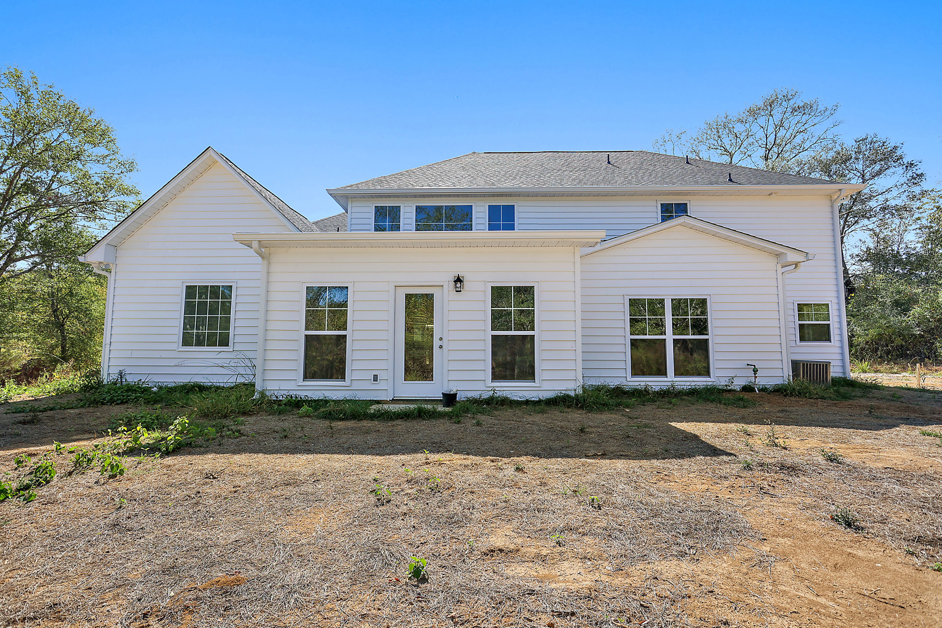 White siding house with multiple square windows, white framed door, exterior lamp, gravel driveway, and trees visible in the background