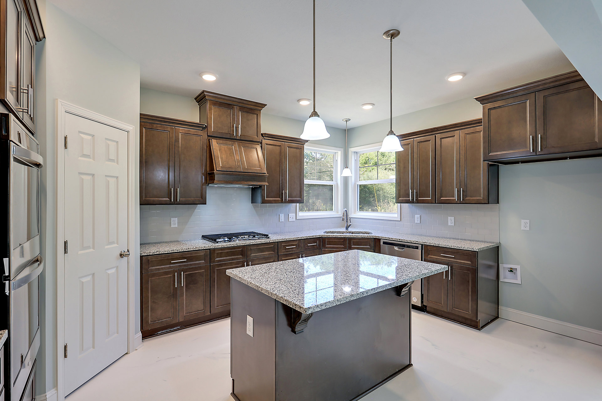 Spacious kitchen featuring a large granite island with built-in sink, white cabinetry, stainless steel appliances, and light-colored walls