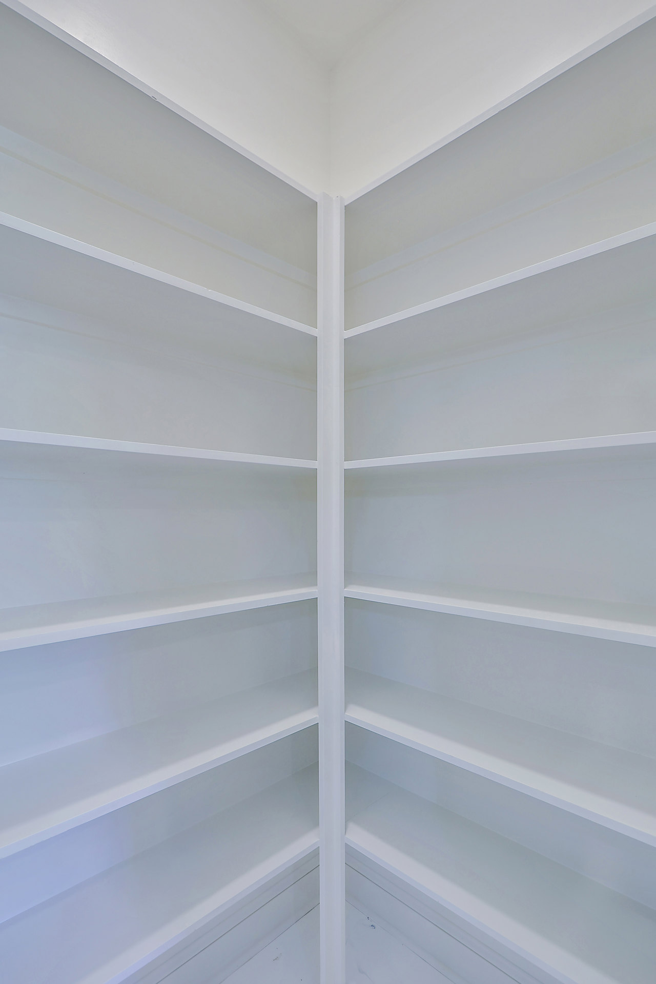 White built-in shelves in the corner of a bright room with white walls and ceiling, window nearby.