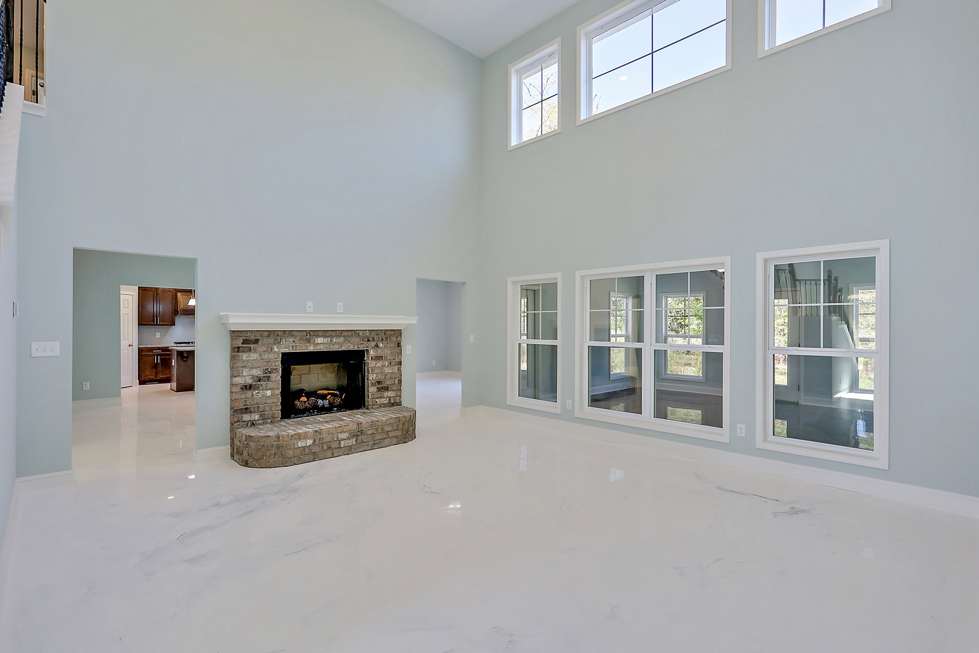 Spacious living room featuring a black-framed brick fireplace with stacked logs, multiple large windows, light hardwood floors, and neutral walls.