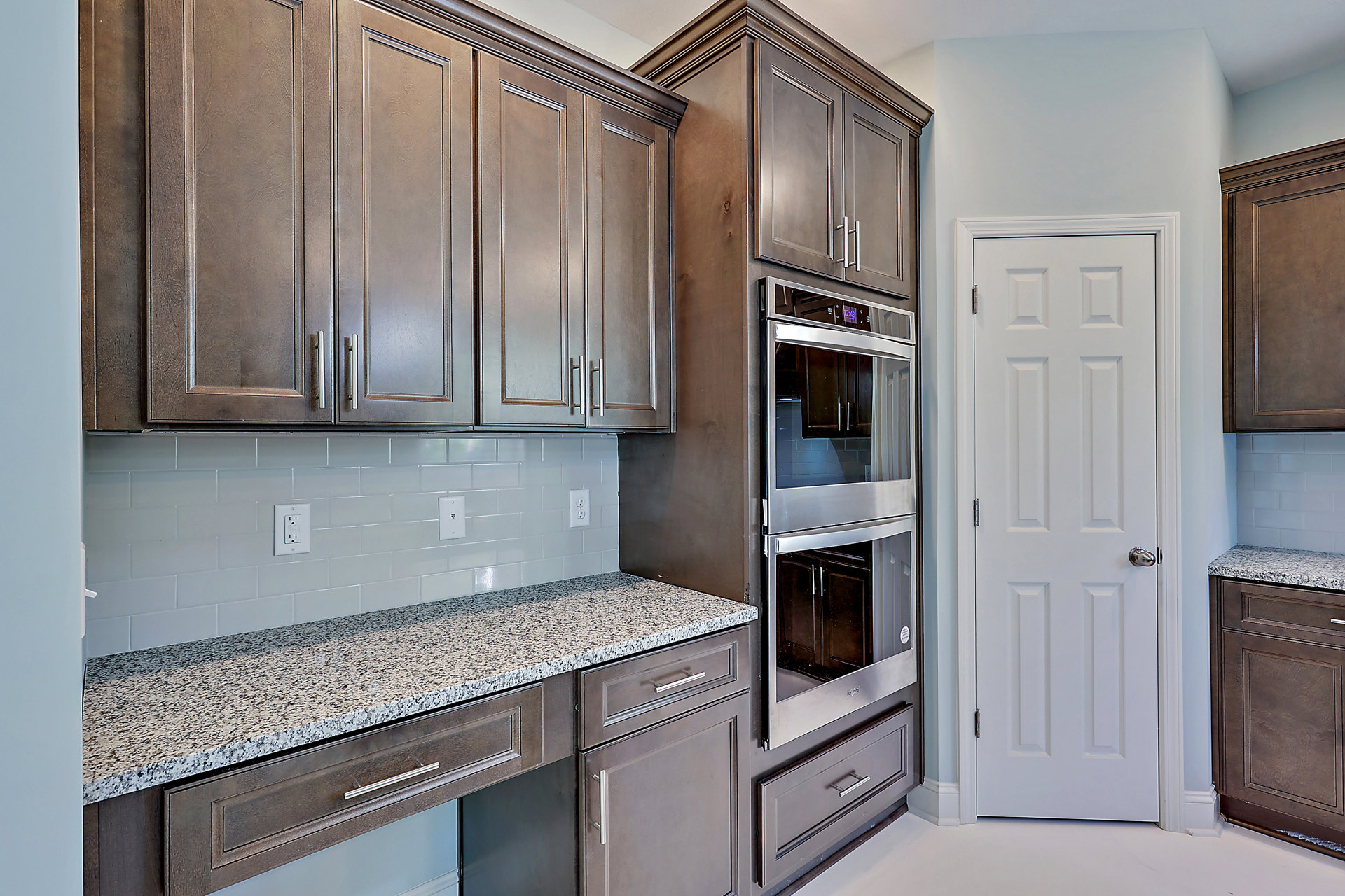 Marble countertop kitchen with white cabinetry, stainless steel oven with glass door, white door featuring silver doorknob, mirrored backsplash, and visible white electrical outlet