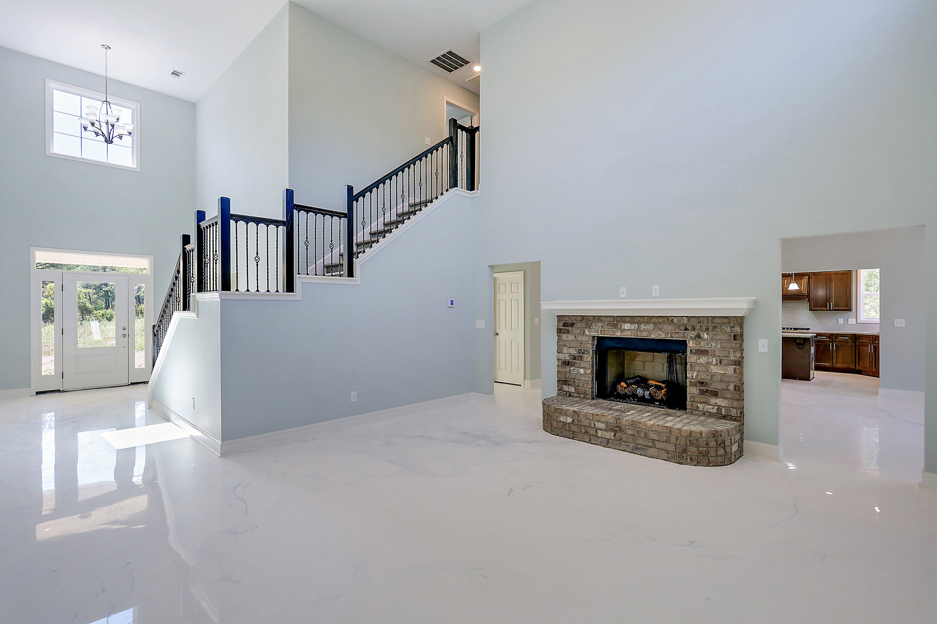 Stone fireplace with stacked logs, white paneled door with silver handle, glass chandelier hanging from ceiling, wooden staircase, plaster walls, hardwood floor