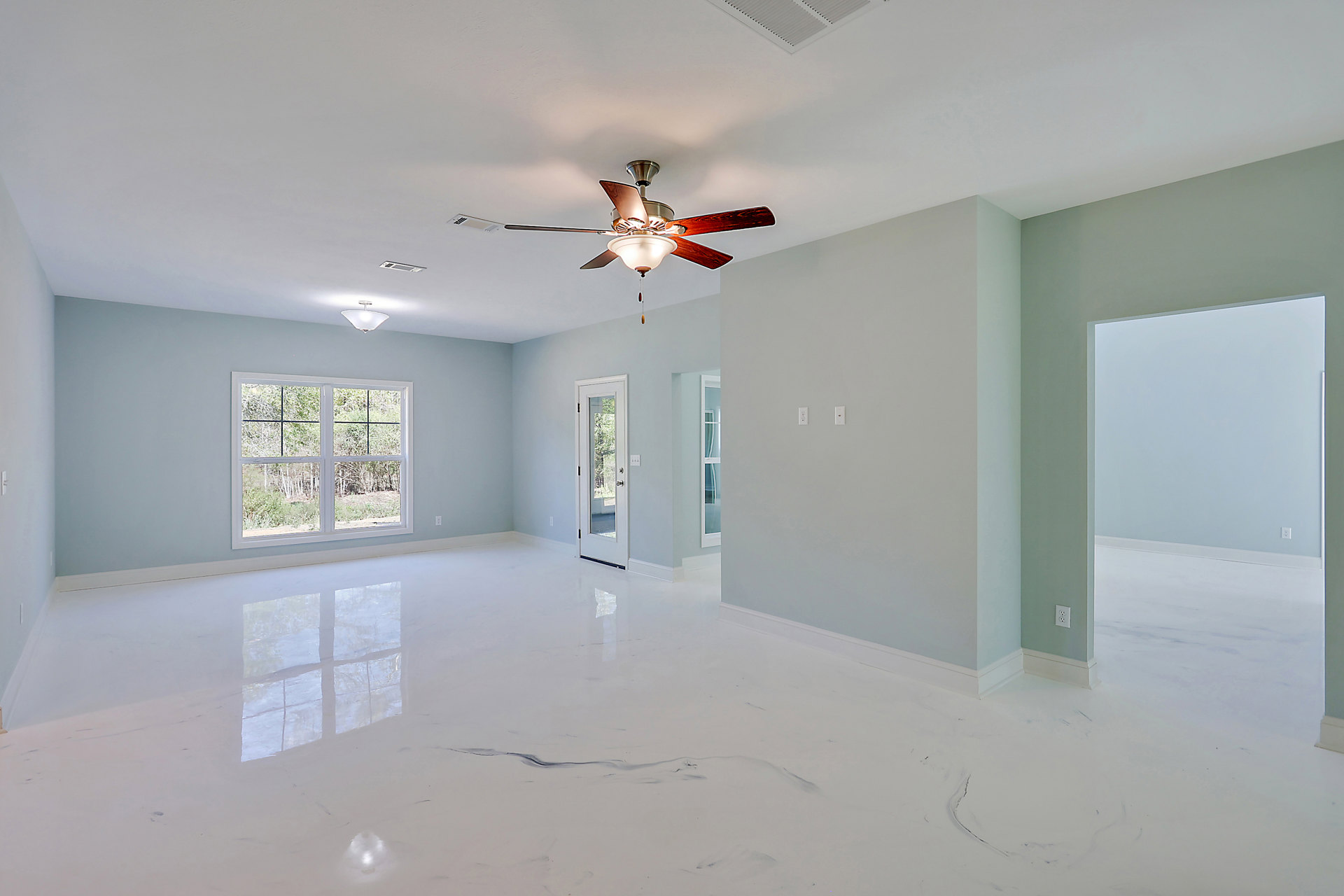 Bright white room with smooth plaster walls, ceiling fan with light fixture, large window overlooking trees and bushes, white door with glass panel, glossy white floor