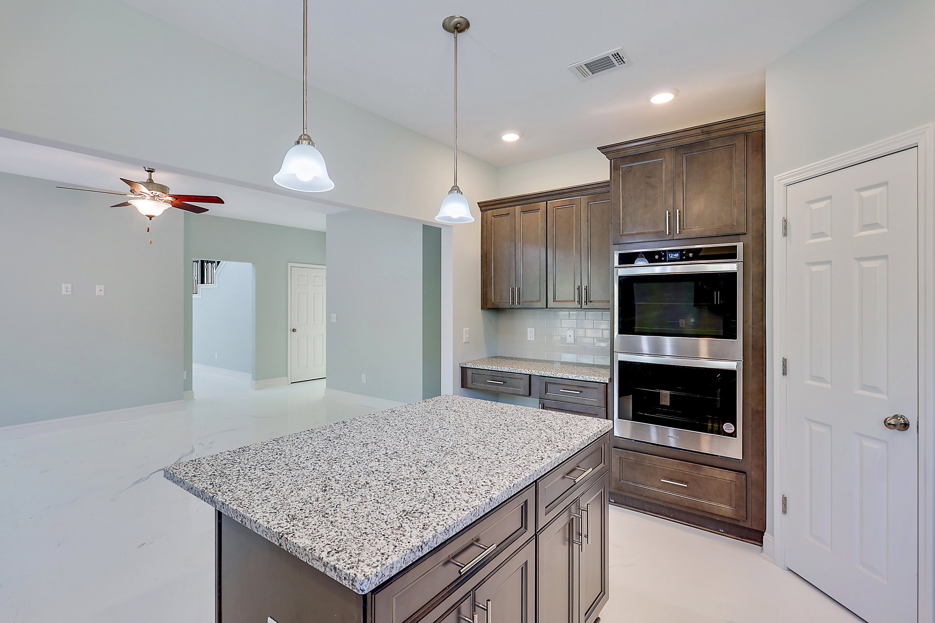 Marble island with white speckled countertop, stainless steel oven with glass door, cabinetry, ceiling fan with light fixture, and silver pendant light in modern kitchen.