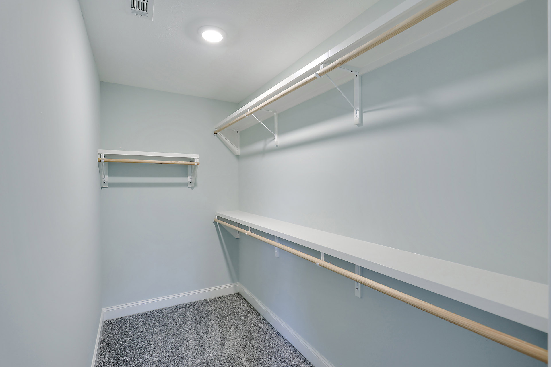 Empty walk-in closet with white shelves, wooden hanging bars, carpeted floor, and recessed ceiling light.