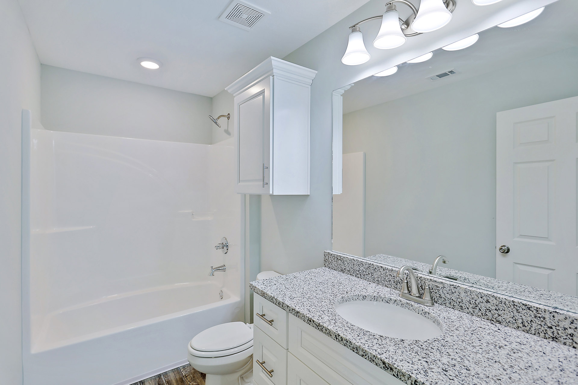 Bathroom with white oval sink and chrome faucet, white toilet with closed lid, glass-enclosed shower featuring metal shower head, light-colored tile walls and floor.