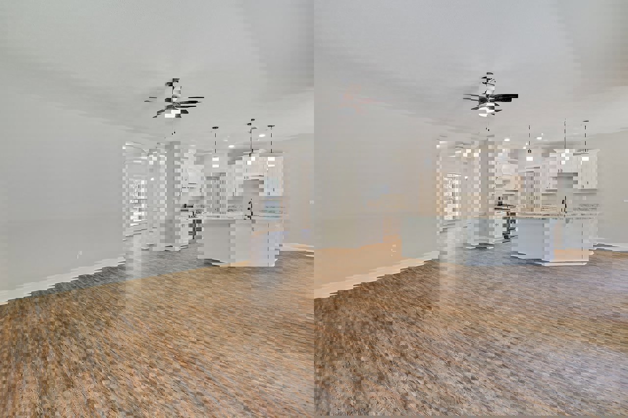 Spacious open floor plan featuring wood flooring, white columns, a kitchen with white cabinets and marble countertop island, ceiling fan with light, dining area, and large window