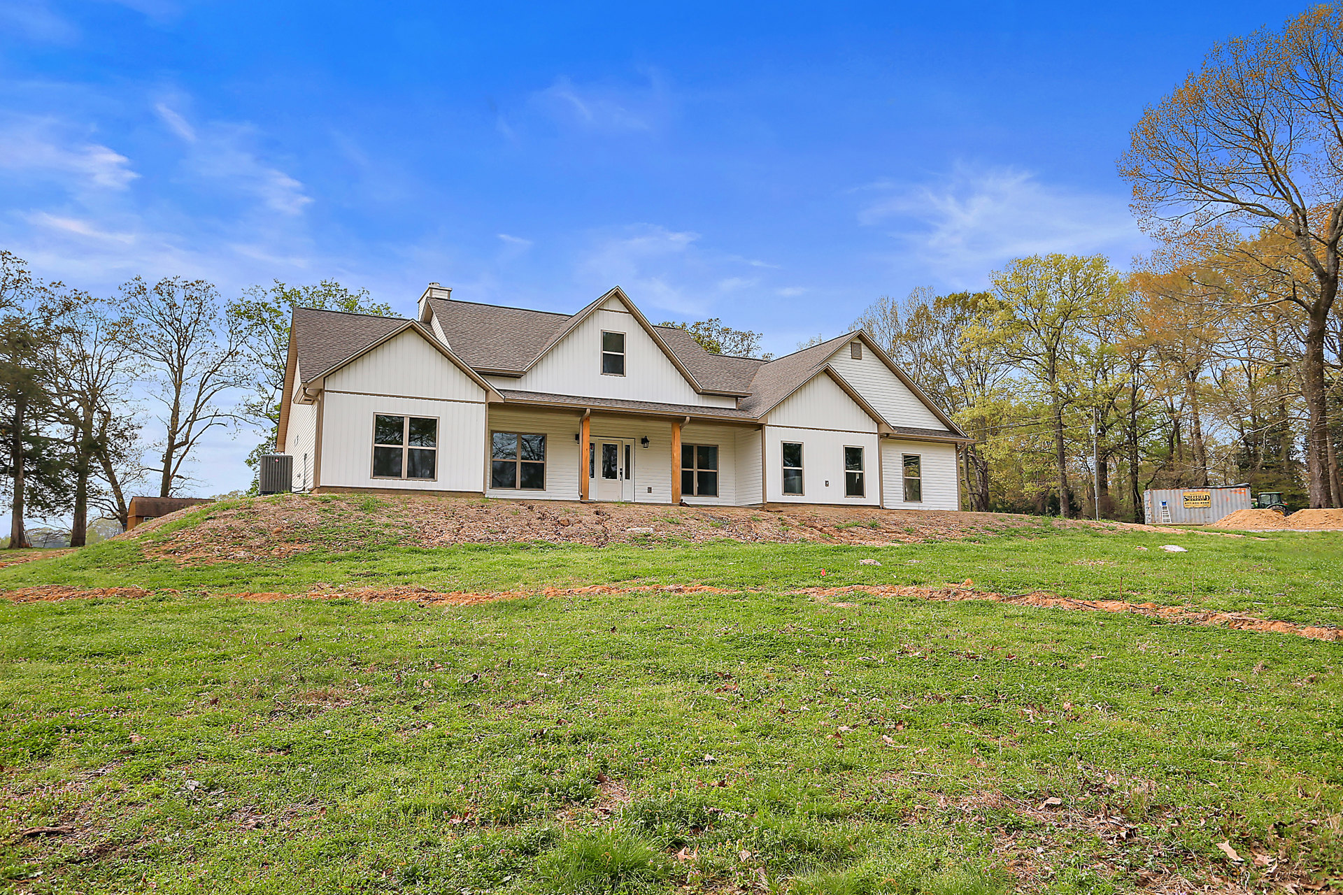 White-roofed house on a grassy hill, large lawn in foreground, wooden-framed windows reflecting nearby trees, cluster of yellow-leaved trees beside home, Robert Frost Farm visible
