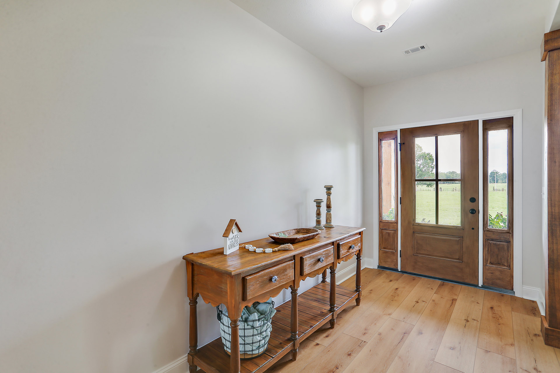 Wooden table with a basket of towels and a bowl, hardwood flooring, wooden door with glass panels, plaster walls, window overlooking fenced grass field