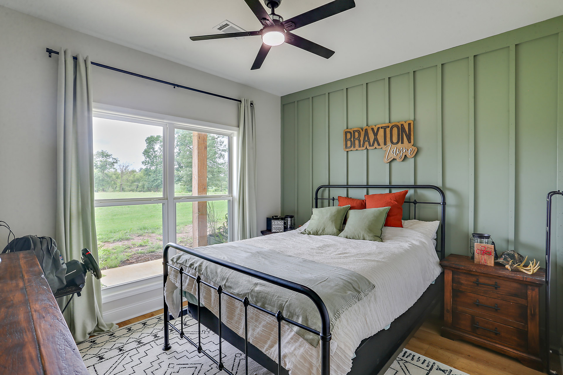 Queen bed with white bedding and pillows, wooden bed frame, ceiling fan with light, dresser topped with antlers and deer skull, decorative sign on wall, neutral walls and carpet
